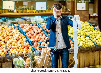 Portrait of an elegant man with shocked emotions holding very long shopping list while buying food in the supermarket