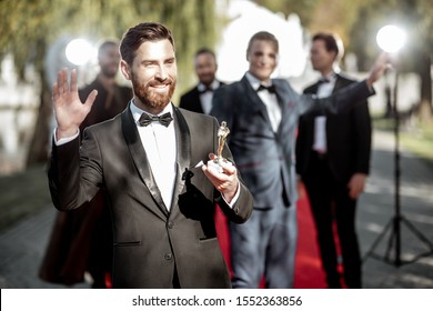 Portrait Of An Elegant Man As A Well-known Movie Actor Holding Famous Academy Award During Awards Ceremony On The Red Carpet Outdoors