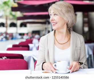 Portrait of elegant mature female who is enjoying of lunch with coffee in cafe.