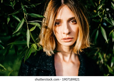 Portrait of elegant stylish blonde short hair girl posing in the park over green branches