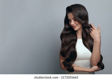 Retrato de elegante y elegante joven mujer con largo cabello brillante y sano y largo maquillaje sobre fondo de banner gris