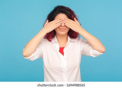 Portrait Of Embarrassed Scared Woman In White Shirt Covering Eyes With Hands So Not To Watch Forbidden Shameful Content, Pretending To Not See Problems. Indoor Studio Shot Isolated On Blue Background