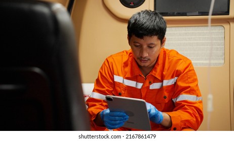 Portrait Of Emergency Medical Technician (EMT) Asian Man Or Paramedic Using Tablet While Sitting In Ambulance Car