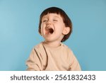 Portrait of emotional little boy on light blue background