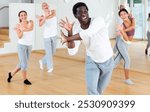 Portrait of emotional young adult man doing exercises during group class in dance center