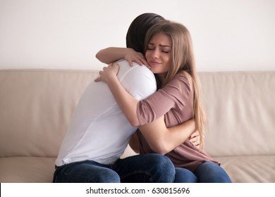 Portrait of emotional young couple hugging each other tightly, boyfriend and girlfriend embracing sitting on couch, reconciliation after argument, love you so much, strong affection in relationships