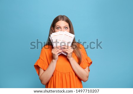 Portrait of emotional young woman with lottery tickets on light blue background