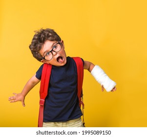 Portrait Of Emotionally Kid Face, Funny Crazy Child Boy With Open Mouth. Pupil In Glasses With Backpack Isolated On Yellow. Back To School. Active Child With Broken Plastered Hand