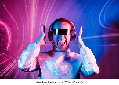 Portrait of emotionally shouting woman in futuristic sunglasses and headphones in pink and blue neon light. Music lover. Silent disco. Woman on background of music vibes background. Futuristic Party