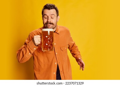 Portrait of emotive handsome man in orange shirt posing with lager foamy beer glass isolated over yellow background. Delightful look. Emotions, beer degustation, facial expression, Oktoberfest concept - Powered by Shutterstock