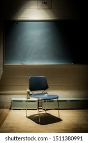 Portrait of an Empty School Chair in a Dark, Shadowy Classroom - in Front of a Chalkboard with a Single Beam of Light Overhead