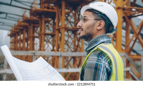 Portrait of engineer planning work at construction site looking at blueprint outdoors in industrial zone. People and occupation concept.