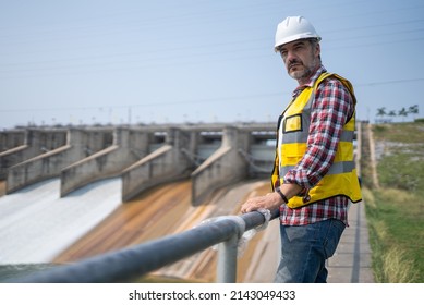 Portrait Of Engineer Wearing Yellow Vest And White Helmet Working Day On A Water Dam With A Hydroelectric Power Plant. Renewable Energy Systems, Sustainable Energy Concept