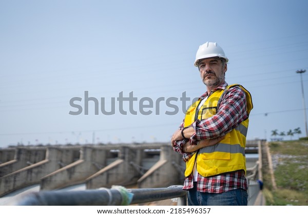 Portrait of engineer\
wearing yellow vest and white helmet Working day on a water dam\
with a hydroelectric power plant. Renewable energy systems,\
Sustainable energy\
concept