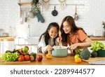 Portrait of enjoy happy love asian family mother with little asian girl daughter child help cooking food healthy eat with vegetable testing smell soup in a pot with spoon.helping mommy in kitchen