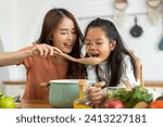 Portrait of enjoy happy love asian family mother with little asian girl daughter child help cooking food healthy eat with fresh vegetable testing smell soup in a pot with spoon.helping mom in kitchen