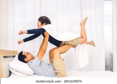 Portrait Of Enjoy Happy Love Asian Family Father Carrying Little Asian Boy Son Smiling Playing Superhero And Having Fun Moments Good Time On Bed At Home