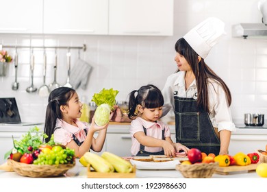 Portrait Of Enjoy Happy Love Asian Family Mother And Little Asian Girl Daughter Child Having Fun Cooking Together With Fresh Vegetable Salad And Sandwich Ingredients On Table In Kitchen