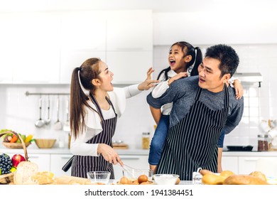Portrait Of Enjoy Happy Love Asian Family Father And Mother With Little Asian Girl Daughter Child Having Fun Cooking Food Together With Baking Cookie And Cake Ingredient On Table In Kitchen