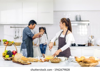 Portrait Of Enjoy Happy Love Asian Family Father And Mother With Little Asian Girl Daughter Child Having Fun Cooking Food Together With Baking Cookie And Cake Ingredient On Table In Kitchen