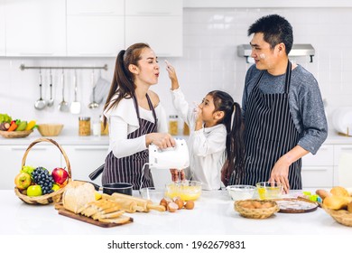 Portrait Of Enjoy Happy Love Asian Family Father And Mother With Little Asian Girl Daughter Child Having Fun Cooking Food Together With Baking Cookie And Cake Ingredient On Table In Kitchen