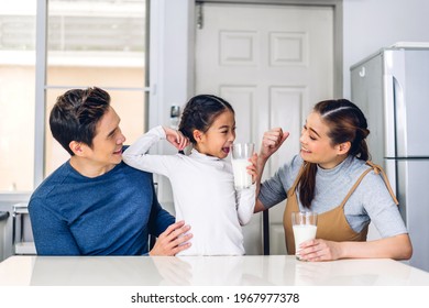 Portrait of enjoy happy love asian family father and mother with little asian girl smiling and having breakfast drinking and hold glasses of milk at table in kitchen