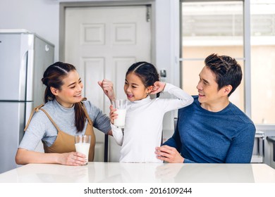 Portrait of enjoy happy love asian family father and mother with little asian girl smiling and having breakfast drinking and hold glasses of milk at table in kitchen