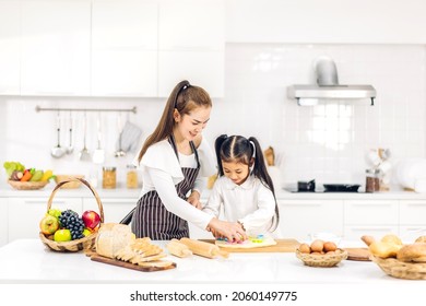 Portrait Of Enjoy Happy Love Asian Family Mother And Little Toddler Asian Girl Daughter Child Having Fun Cooking Together With Dough For Homemade Bake Cookie And Cake Ingredient On Table In Kitchen