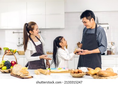 Portrait Of Enjoy Happy Love Asian Family Father And Mother With Little Asian Girl Daughter Child Play And Having Fun Cooking Food Together With Baking Cookie And Cake Ingredient In Kitchen