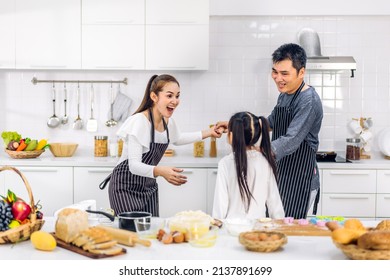 Portrait Of Enjoy Happy Love Asian Family Father And Mother With Little Asian Girl Daughter Child Play And Having Fun Cooking Food Together With Baking Cookie And Cake Ingredient In Kitchen