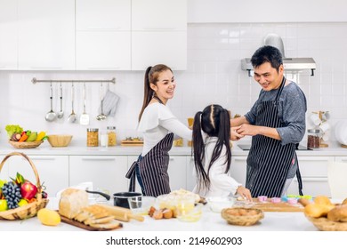 Portrait Of Enjoy Happy Love Asian Family Father And Mother With Little Asian Girl Daughter Child Play And Having Fun Cooking Food Together With Baking Cookie And Cake Ingredient In Kitchen