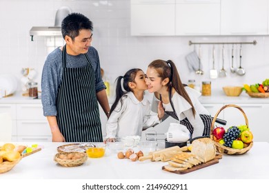 Portrait Of Enjoy Happy Love Asian Family Father And Mother With Little Asian Girl Daughter Child Play And Having Fun Cooking Food Together With Baking Cookie And Cake Ingredient In Kitchen