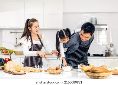 Portrait Of Enjoy Happy Love Asian Family Father And Mother With Little Asian Girl Daughter Child Play And Having Fun Cooking Food Together With Baking Cookie And Cake Ingredient In Kitchen