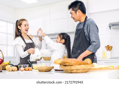 Portrait Of Enjoy Happy Love Asian Family Father And Mother With Little Asian Girl Daughter Child Play And Having Fun Cooking Food Together With Baking Cookie And Cake Ingredient In Kitchen