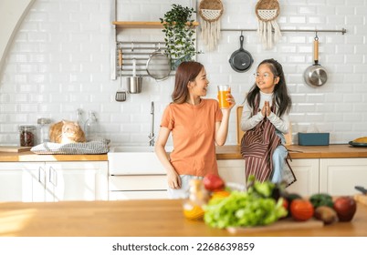 Portrait of enjoy happy love asian family mother with little asian girl preparing drinking glass of fresh juice and orange on counter in kitchen at home.Diet concept.healthy drink - Powered by Shutterstock