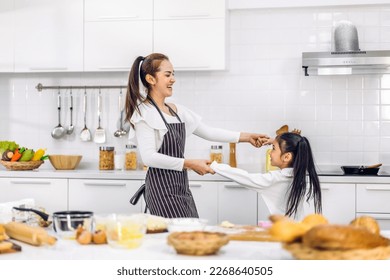 Portrait of enjoy happy love asian family mother and little toddler asian girl daughter child having fun cooking together with dough for homemade bake cookie and cake ingredient on table in kitchen - Powered by Shutterstock