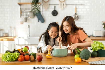 Portrait of enjoy happy love asian family mother with little asian girl daughter child help cooking food healthy eat with vegetable testing smell soup in a pot with spoon.helping mommy in kitchen - Powered by Shutterstock