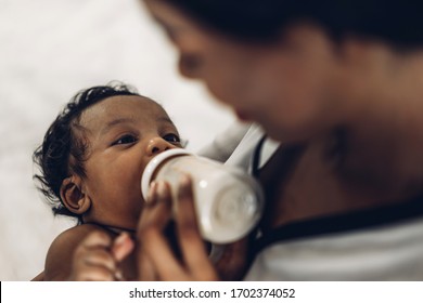 Portrait of enjoy happy love family african american mother playing with adorable little african american baby.Mom feeding bottle of milk to baby cute son in a white  bedroom.Love of black family 