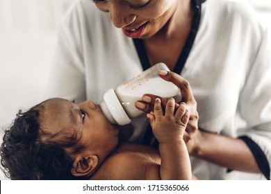 Portrait Of Enjoy Happy Love Family African American Mother Playing With Adorable Little African American Baby.Mom Feeding Bottle Of Milk To Baby Cute Son In A White  Bedroom.Love Of Black Family 