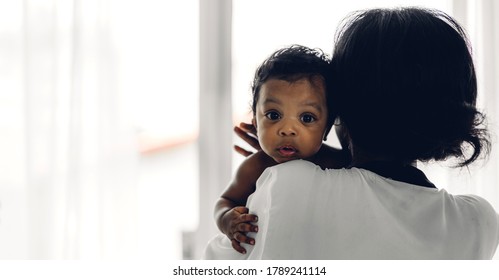Portrait of enjoy happy love family african american mother playing with adorable little african american baby.Mom touching with cute son moments good time in a white bedroom.Love of black family 