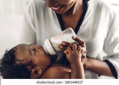 Portrait Of Enjoy Happy Love Family African American Mother Playing With Adorable Little African American Baby.Mom Feeding Bottle Of Milk To Baby Cute Son In A White  Bedroom.Love Of Black Family 