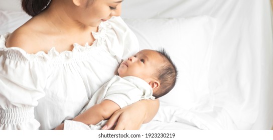 Portrait of enjoy happy love family asian mother playing with adorable little asian baby.Mom touching with cute son moments good time in a white bedroom.Love of family concept