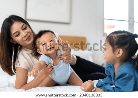 Portrait of enjoy happy love family asian mother playing with adorable little asian baby and sister girl, newborn, infant.Mom touching care with cute son in a white bedroom.Love of family concept