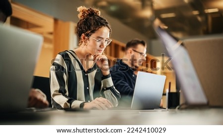 Portrait of Enthusiastic Hispanic Young Woman Working on Computer in a Modern Bright Office. Confident Human Resources Agent Smiling Happily While Collaborating Online with Colleagues. Foto d'archivio © 