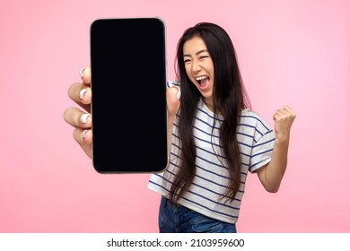 Portrait of euphoric happy joyful girl with long hair screaming with happiness showing mobile advertisement mockup area and celebrating her victory. indoor studio shot isolated on pink background - Shutterstock ID 2103959600