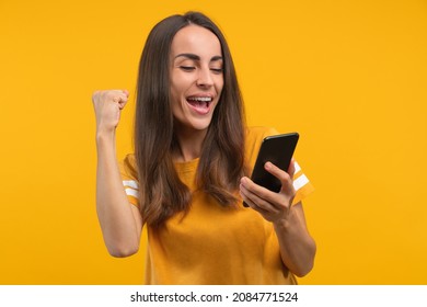 Portrait Of Euphoric Young Woman With A Phone In Hands Celebrating Success, Jackpot In Online Lottery Or Money Win At Bookmaker's Mobile Application, Her Bet Played.