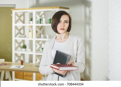 Portrait Of European Woman Holding Closed Book In Modern Office Interior. Knowledge And Information Concept 