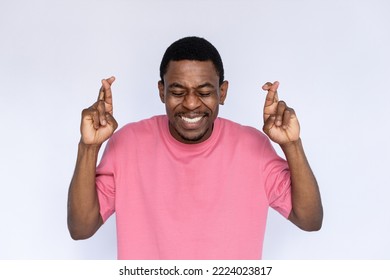 Portrait of excited African American man crossing fingers. Happy young male model with short dark hair in pink T-shirt with closed eyes smiling while making a wish. Luck, superstition concept - Shutterstock ID 2224023817
