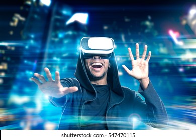 Portrait Of An Excited African American Man In Virtual Reality Glasses Playing A Game In A Night City. Toned Image. Double Exposure