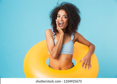 Portrait of an excited african girl dressed in swimsuit holding infatable ring isolated over blue background